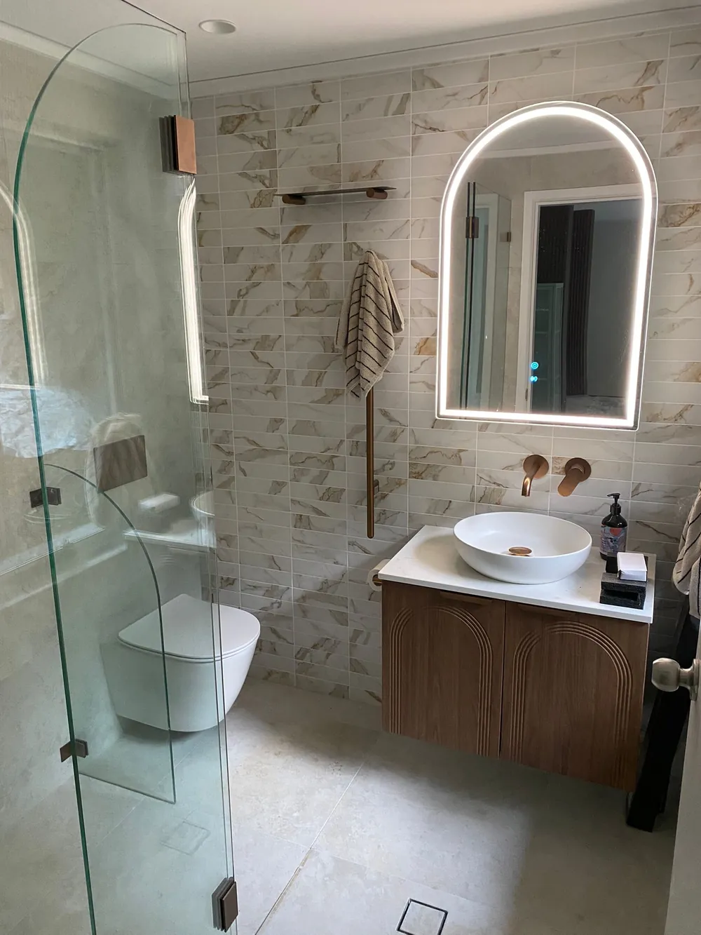 Full bathroom renovation with arched LED mirror, stone-look walls and a fluted timber vanity