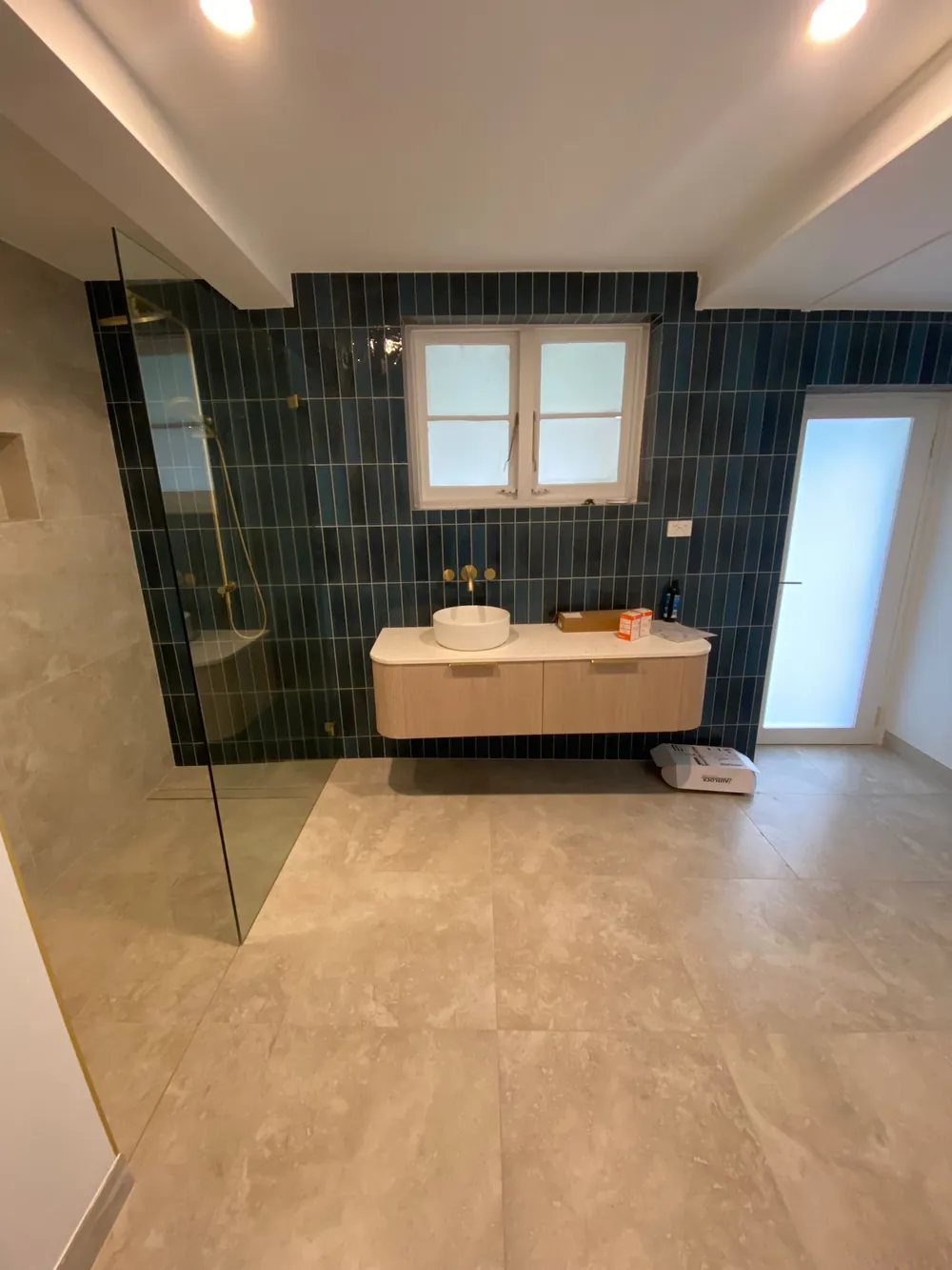 Wide bathroom with deep green vertical tiles, twin basin timber vanity and frameless shower screen