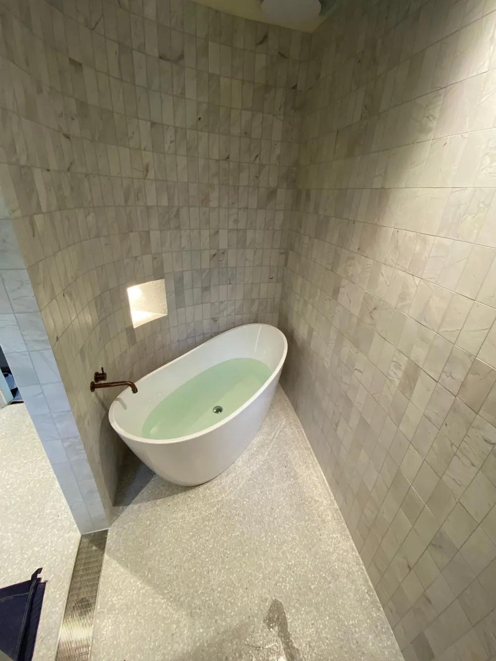 Freestanding bath against a stone-look wall with a terrazzo floor and lit niche