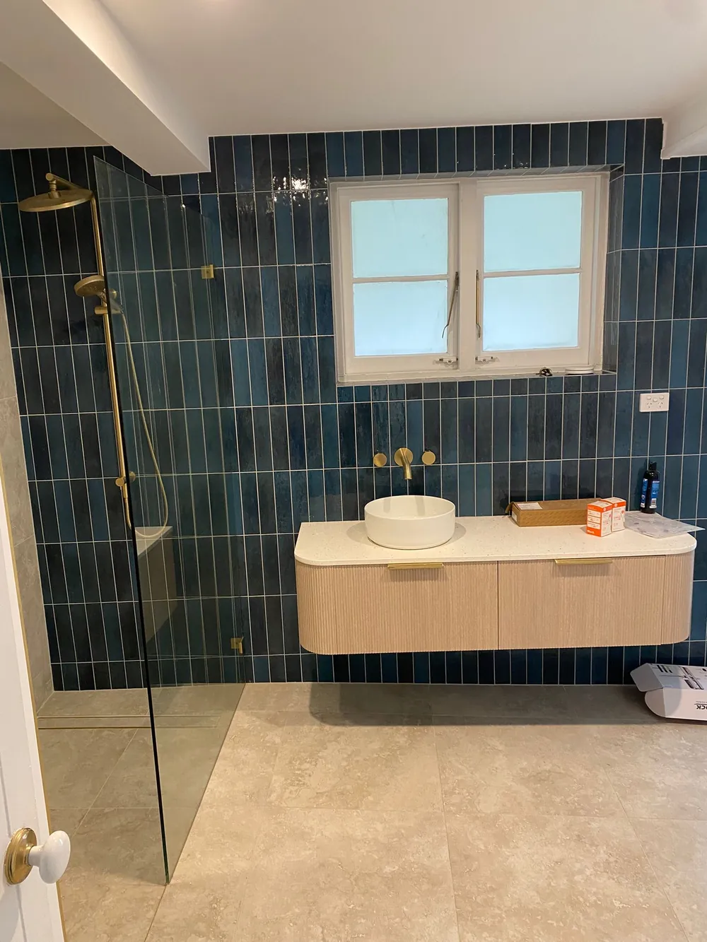 Brushed brass tapware and shower against deep green vertical tiles