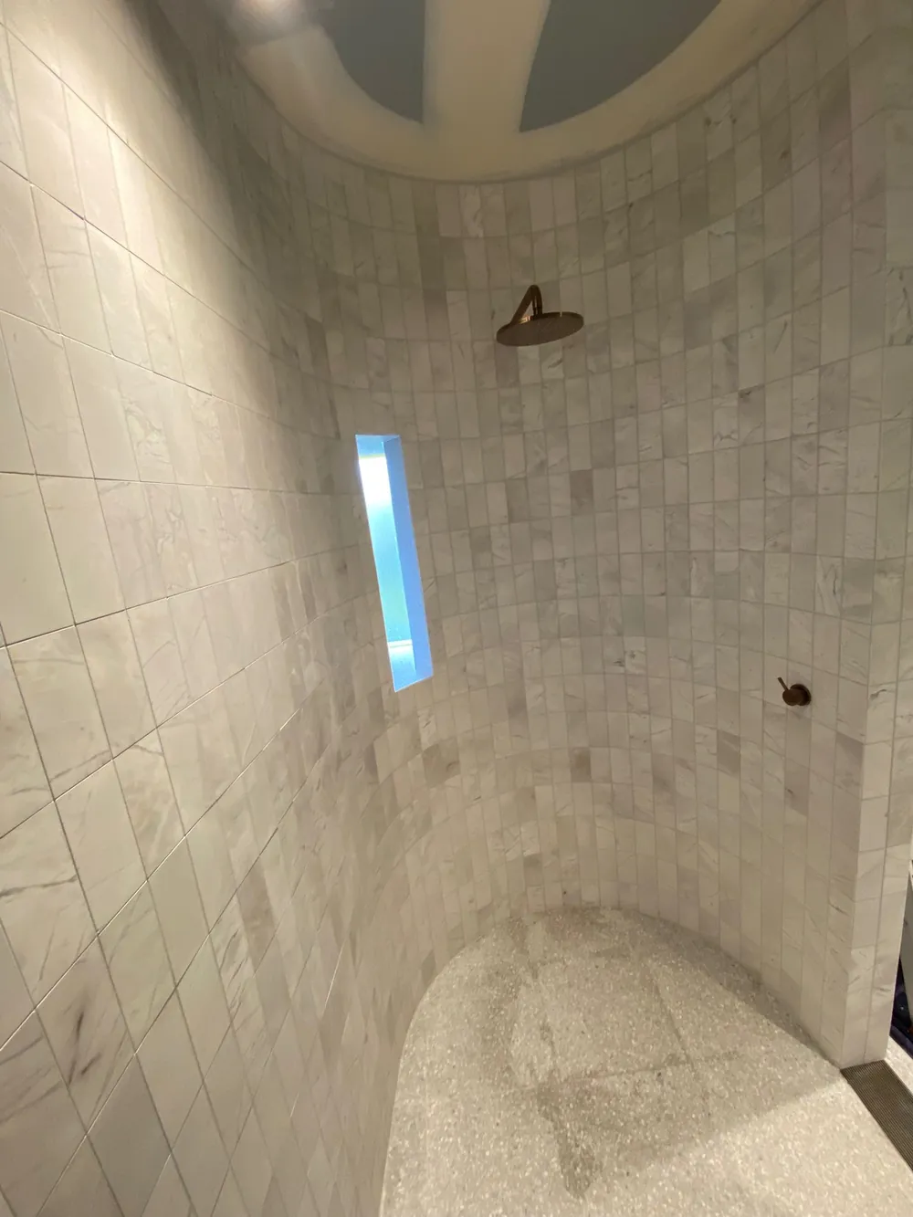 Walk-in shower in marble-look tile with a slim vertical window and stone floor