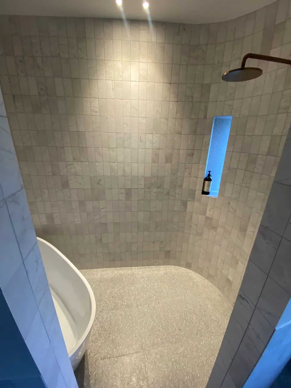 Shower recess beside a freestanding bath, in marble-look tile with aged brass tapware